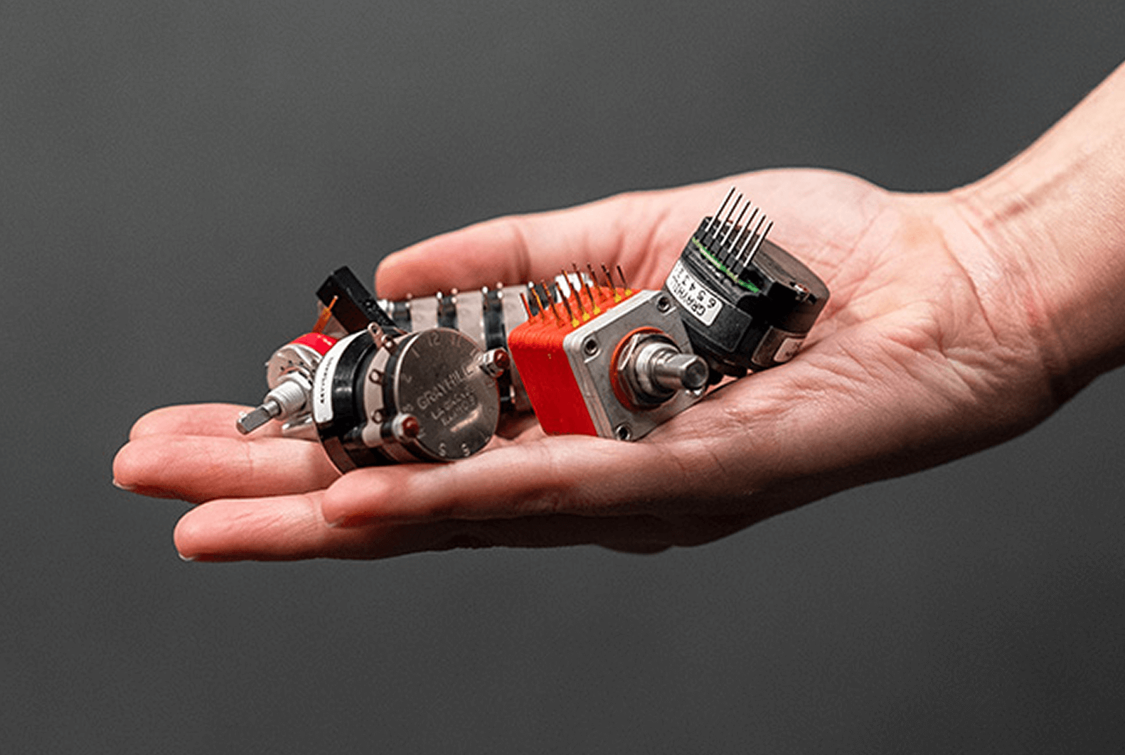 An open hand holding a variety of Grayhill rotary switches and encoders, showcasing a range of different models and sizes.